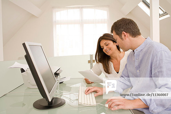 Reife Paare die Rechnungen und Papierkram auf dem heimischen Desktop-Computer prüfen.