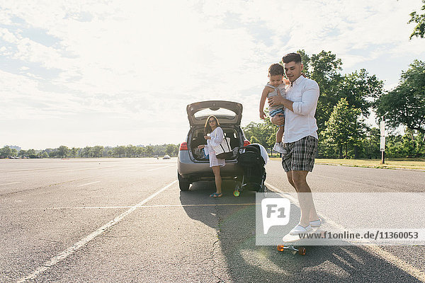 Young man carrying toddler son whilst skateboarding Pelham Bay Park Bronx New York USA