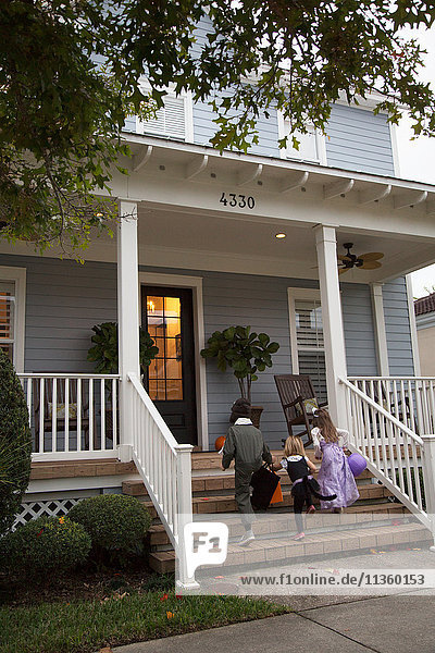 Boy and sisters trick or treating moving up porch stairway