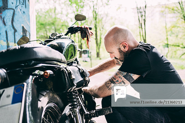 Mature male motorcyclist crouching to repair motorcycle