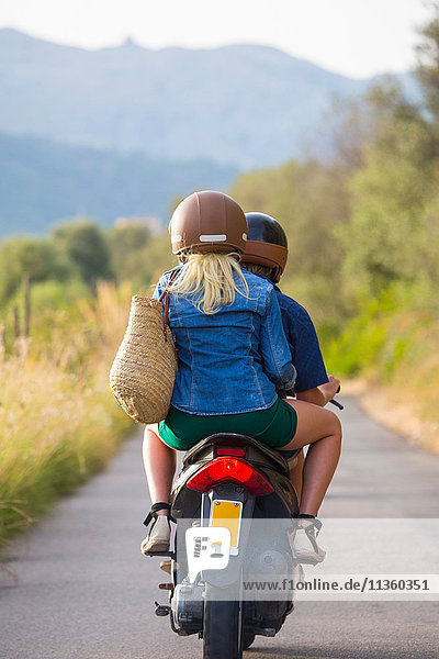 Rückansicht eines jungen Paares beim Mopedfahren auf einer Landstraße  Mallorca  Spanien