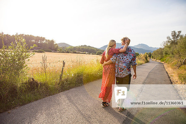 Rückansicht eines romantischen jungen Paares bei einem Spaziergang entlang einer Landstraße  Mallorca  Spanien