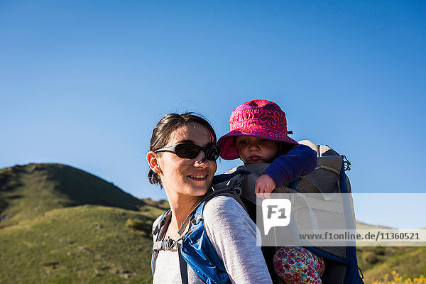Mother carrying young daughter on back  hiking the Bonneville Shoreline Trail in the Wasatch Foothills above Salt Lake City  Utah  USA