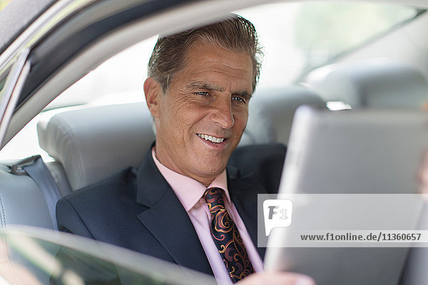 Ein reifer Geschäftsmann auf dem Rücksitz eines Autos  der ein digitales Tablet benutzt