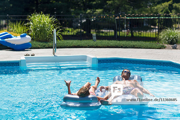 Mature couple in swimming pool relaxing on inflatables