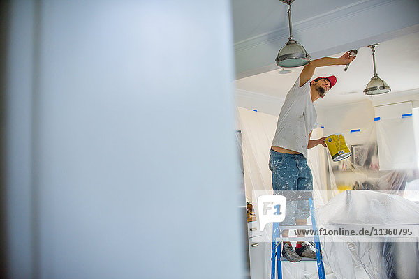 Man up stepladder painting ceiling