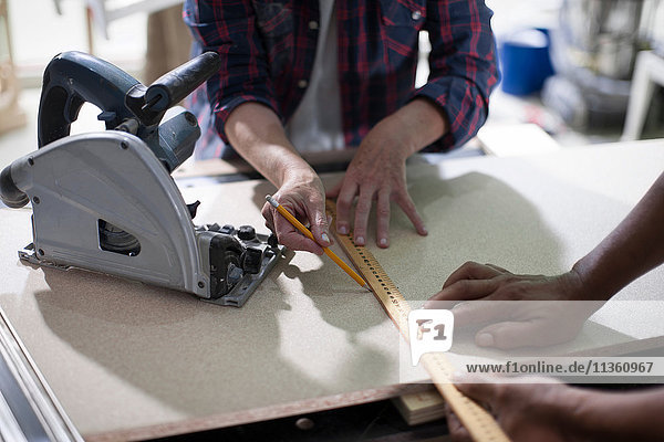 Ausschnitt eines Schnappschusses von Tischlern  die in einer Möbelbauwerkstatt Messungen vornehmen