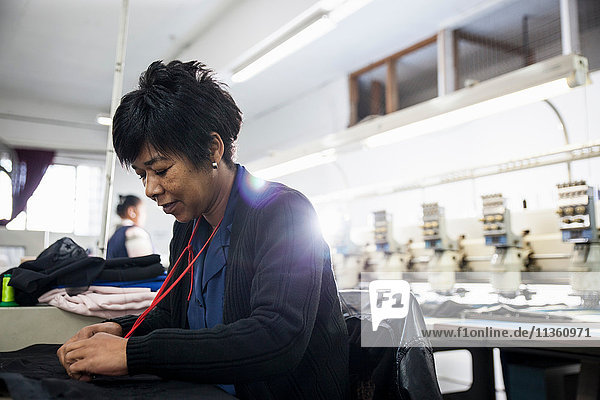 Female factory worker removing stitches from black cloth from speed stitching programmed embroidery machine in clothing factory