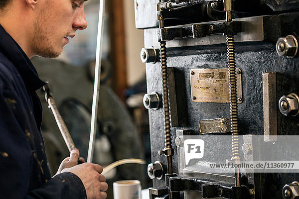 Junger männlicher Drucker bei der Bedienung von Druckmaschinen in der Druckereiwerkstatt