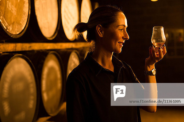 Weibliche Verkosterin betrachtet die Farbe von Whisky im Glas in der Whisky-Destillerie
