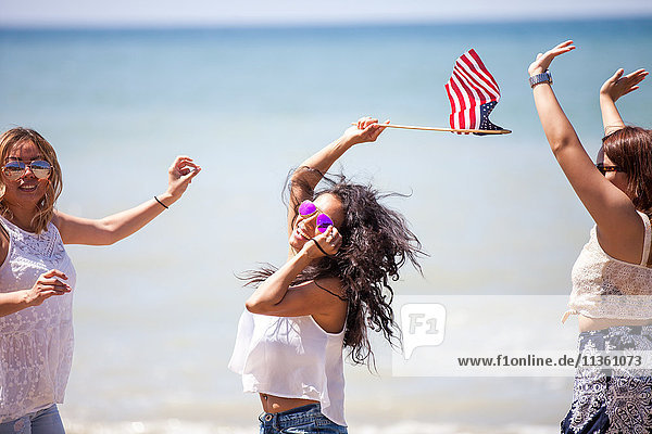 Three adult female friends waving American flag on beach  Malibu  California  USA