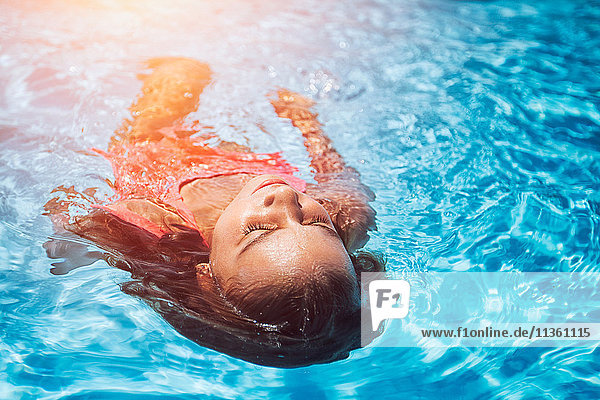 Girl floating on her back in sunlit swimming pool