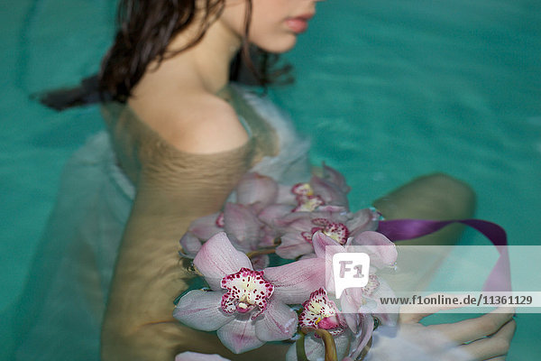 Schnappschuss einer jungen Frau im Schwimmbad des Kurortes mit einem Strauss violetter Orchideen