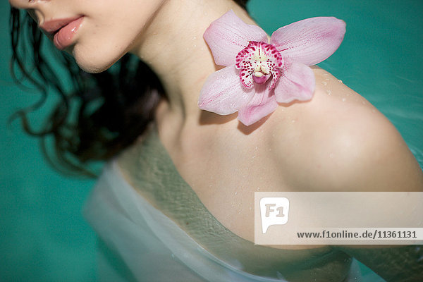 Nahaufnahme einer jungen Frau im Whirlpool mit lila Orchidee auf der nackten Schulter
