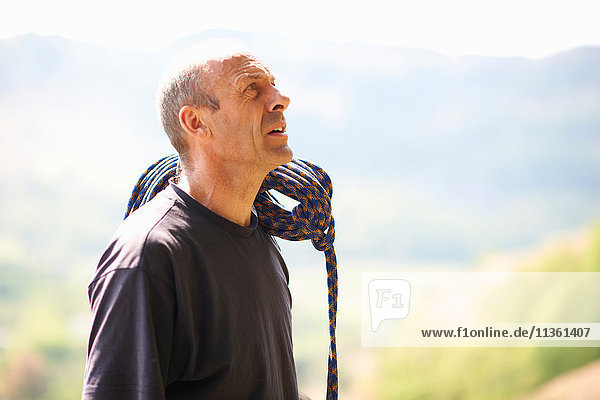 Rock climber carrying rope on shoulder looking up