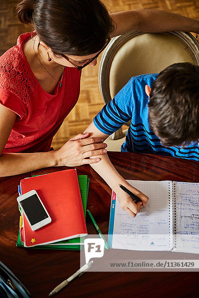 Schrägansicht der Mutter am Esstisch  die dem Sohn bei den Hausaufgaben hilft