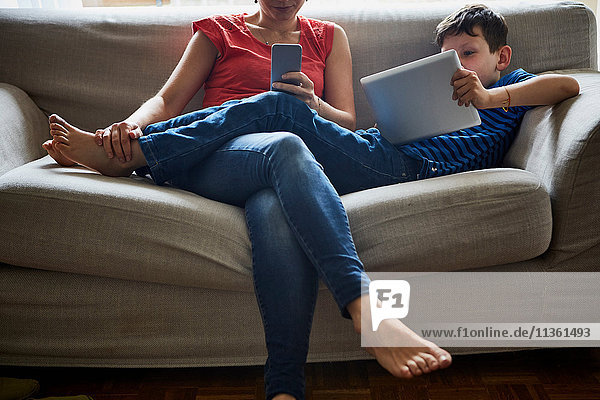 Mutter und Sohn entspannen sich auf dem Sofa mit digitalem Tablet und Smartphone