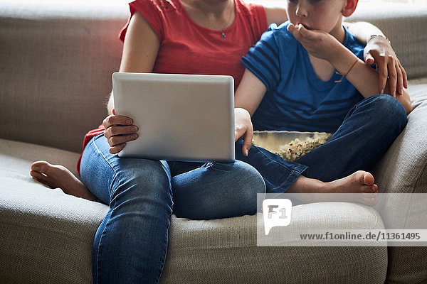 Geschnittene Ansicht von Mutter und Sohn auf dem Sofa mit Popcorn per Smartphone