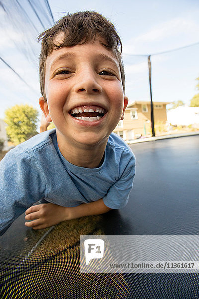 Porträt eines Jungen  der sich auf einem großen Trampolin abstützt und lacht