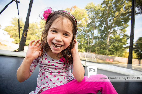 Porträt eines jungen Mädchens  das auf einem großen Trampolin sitzt und lacht