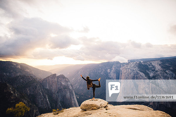Junge Frau steht in Yoga-Pose auf dem Gipfel eines Berges mit Blick auf den Yosemite-Nationalpark Kalifornien USA