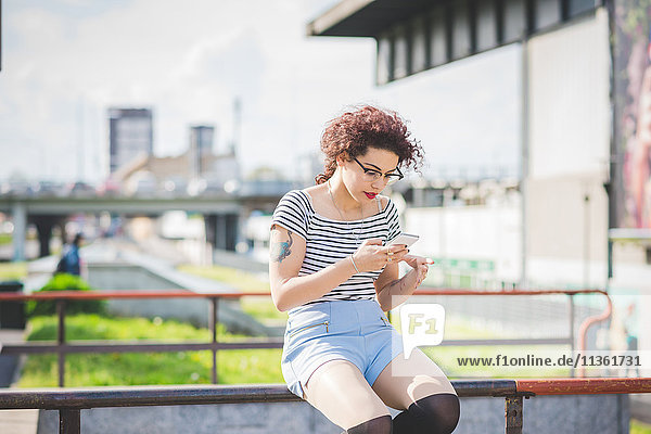 Woman sitting in urban area texting on smartphone  Milan  Italy