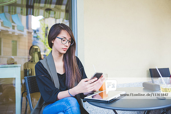 Junge Frau liest im Straßencafé Smartphone-Texte