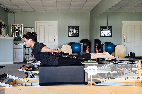 Side view of woman in gym using pilates reformer