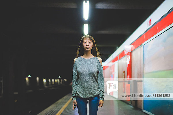 Porträt einer jungen Frau  die nachts auf dem Bahnsteig steht und auf den Bahnsteig starrt