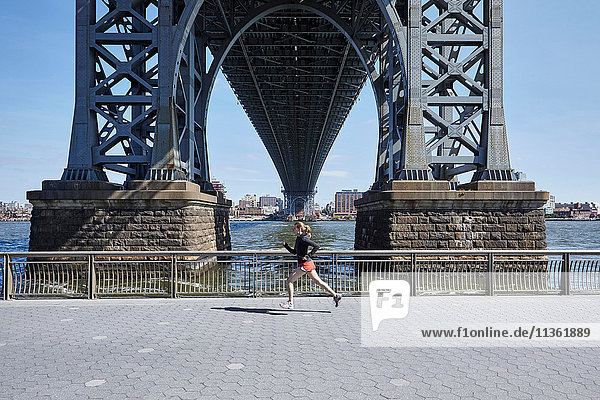Junge Frau  die im Freien trainiert und unter der Williamsburg Bridge läuft  New York City  USA
