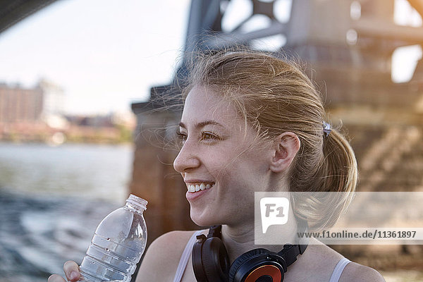 Junge Frau am Fluss  trägt Kopfhörer um den Hals  hält Wasserflasche  New York City  USA