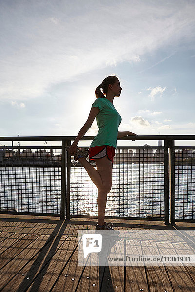 Seitenansicht einer Frau  die ihr Bein am Pier streckt  Manhattan  New York  USA