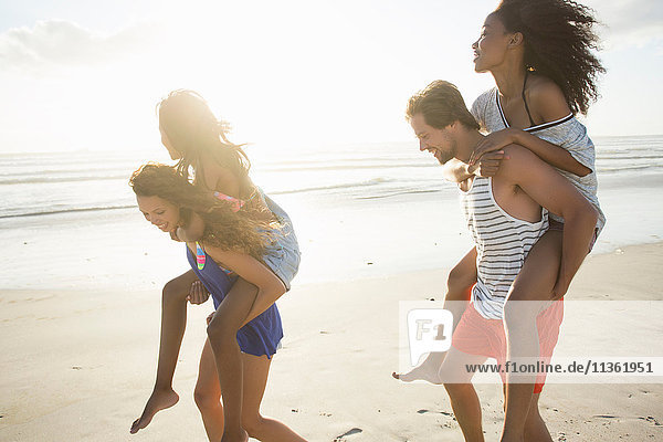 Young man and woman piggybacking friends in beach race  Cape Town  South Africa