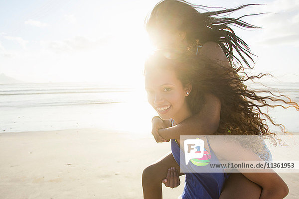 Porträt einer jungen Frau  die eine Freundin am Strand huckepack nimmt  Kapstadt  Südafrika