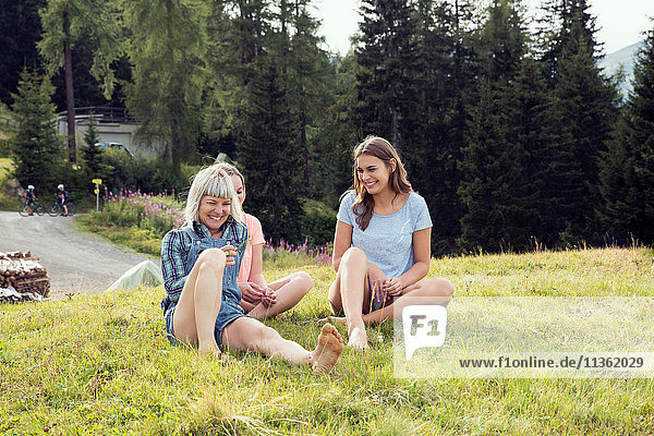 Drei erwachsene Freundinnen sitzen lachend auf dem Feld  Sattelbergalm  Tirol  Österreich