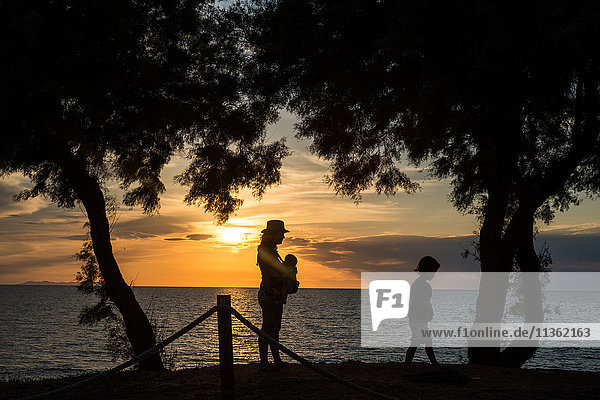 Silhouette of mother and children by water at sunset  Italy