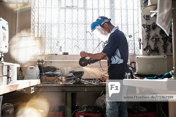 Junger Mann mit Winkelschleifer am Schraubstock in der Reparaturwerkstatt