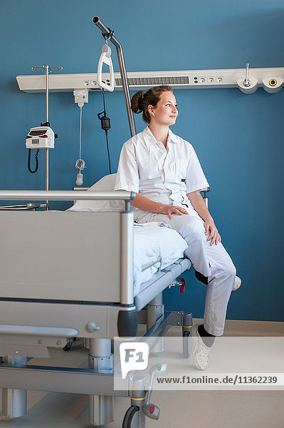 Krankenschwester sitzt auf einem Krankenhausbett und schaut weg