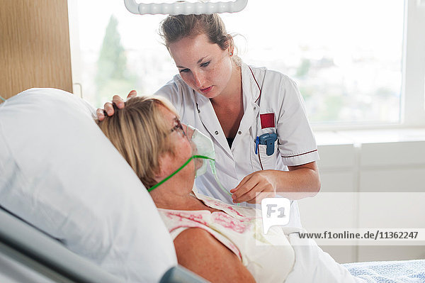 Krankenschwester  die den Patienten im Krankenhausbett mit Sauerstoffmaske pflegt