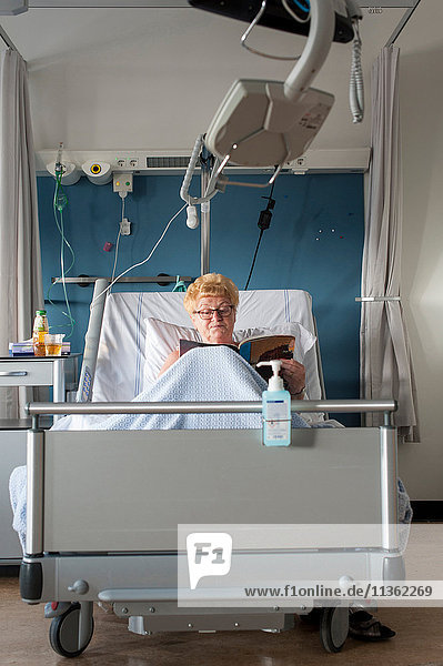 Patient im Krankenhausbett liest Zeitschrift