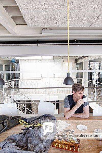 Fashion designer at table holding tea cup looking away