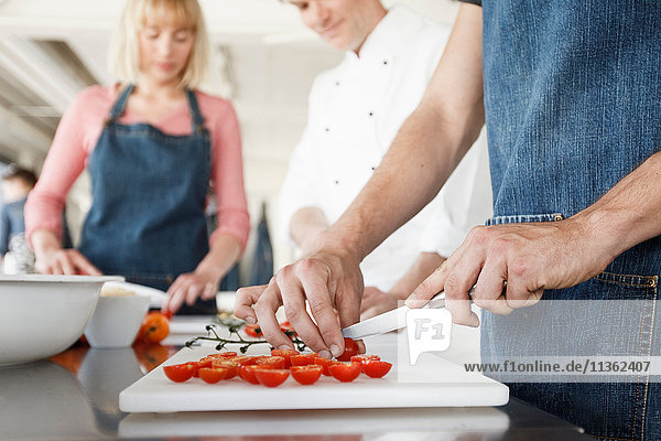 Koch und Ehepaar in der Küche schneiden Tomaten in Scheiben