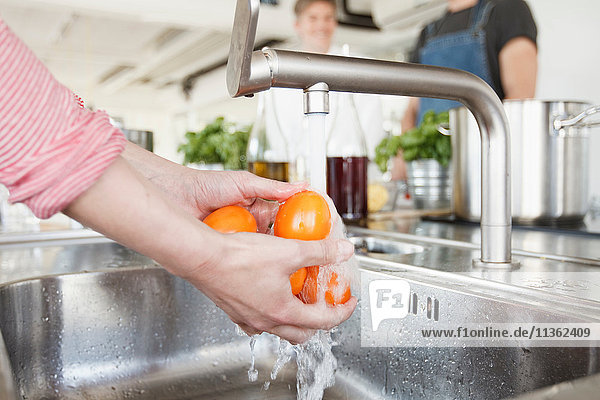 Cropped view of woman's hands washing tomatoes under tap
