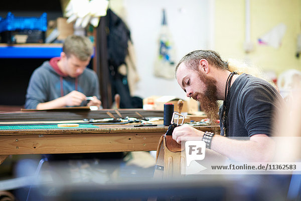 Male worker in leather workshop  sewing up seams around a belt buckle