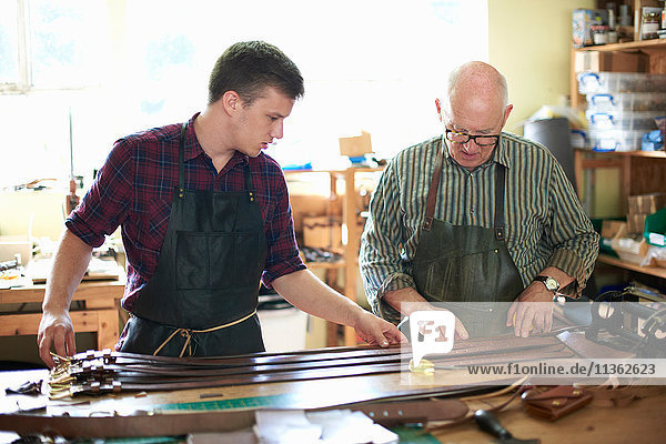 Zwei männliche Arbeiter in Lederwerkstatt bei der Kontrolle von Ledergürteln