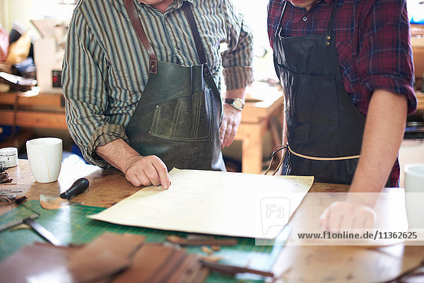 Zwei männliche Arbeiter in der Lederwerkstatt  Blick auf die Pläne  mittlerer Abschnitt