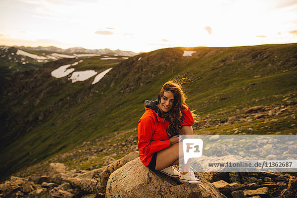 Frau sitzt auf einem Felsen und schaut lächelnd in die Kamera  Rocky Mountain National Park  Colorado  USA