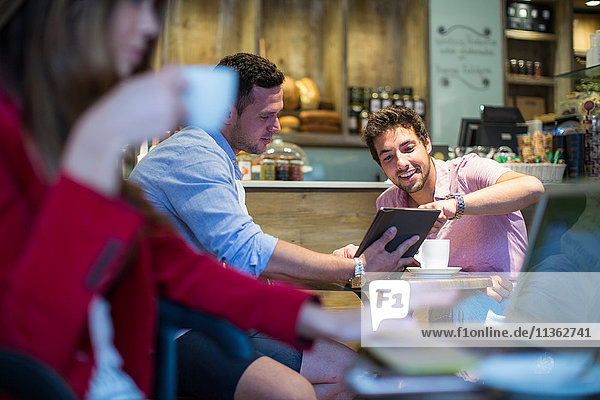 Male friends sitting in cafe pointing at digital tablet