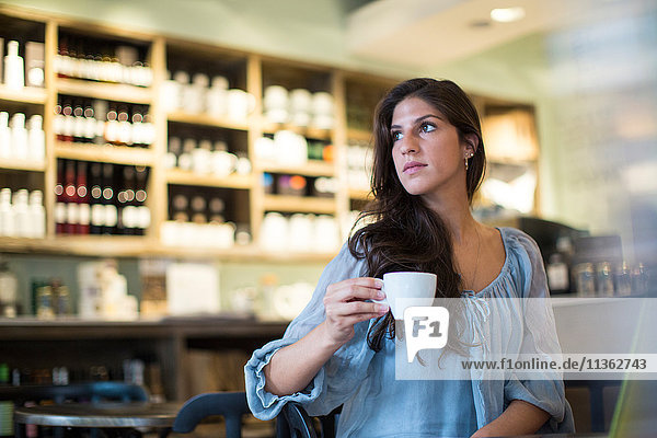 Junge Frau sitzt im Cafe und schaut zur Seite
