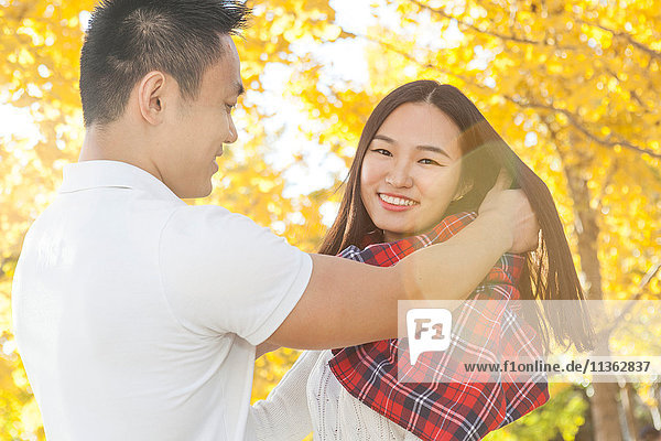 Junger Mann wickelt Tartan-Schal um seine Freundin im Herbstpark  Peking  China